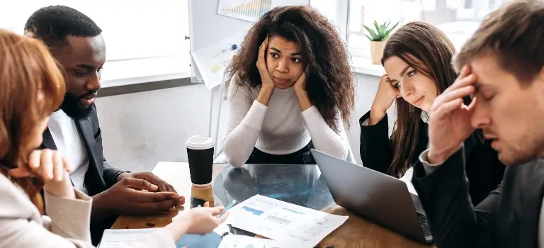 A team of people sitting around a table at work and looking stressed.